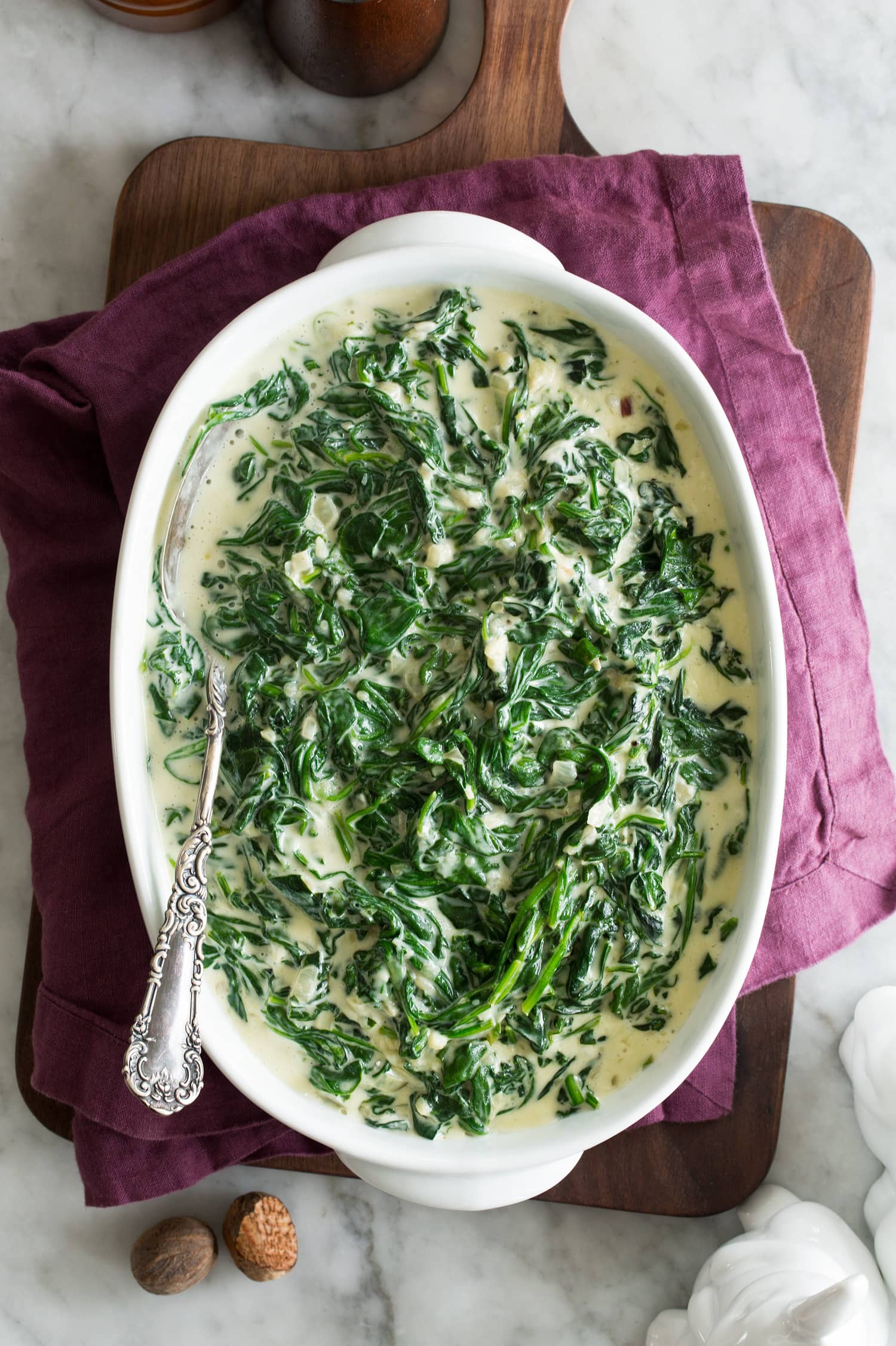Creamed Spinach Fresh creamed spinach in a white oval serving dish set over a purple cloth and a wooden tray.