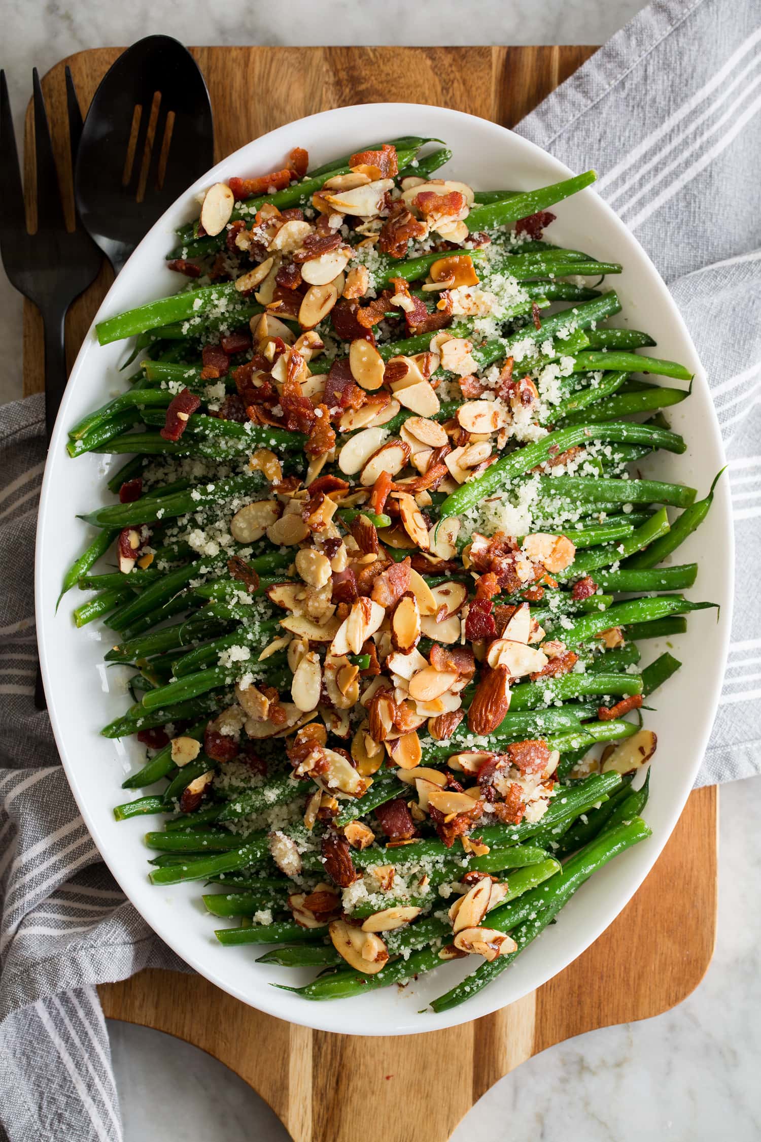 Green Bean Almondine Beautiful Green Bean Almondine. Sauteed green beans are shown lined up in a row on a platter with toasted almonds, crumbled fried bacon and grated parmesan are sprinkled over the top.