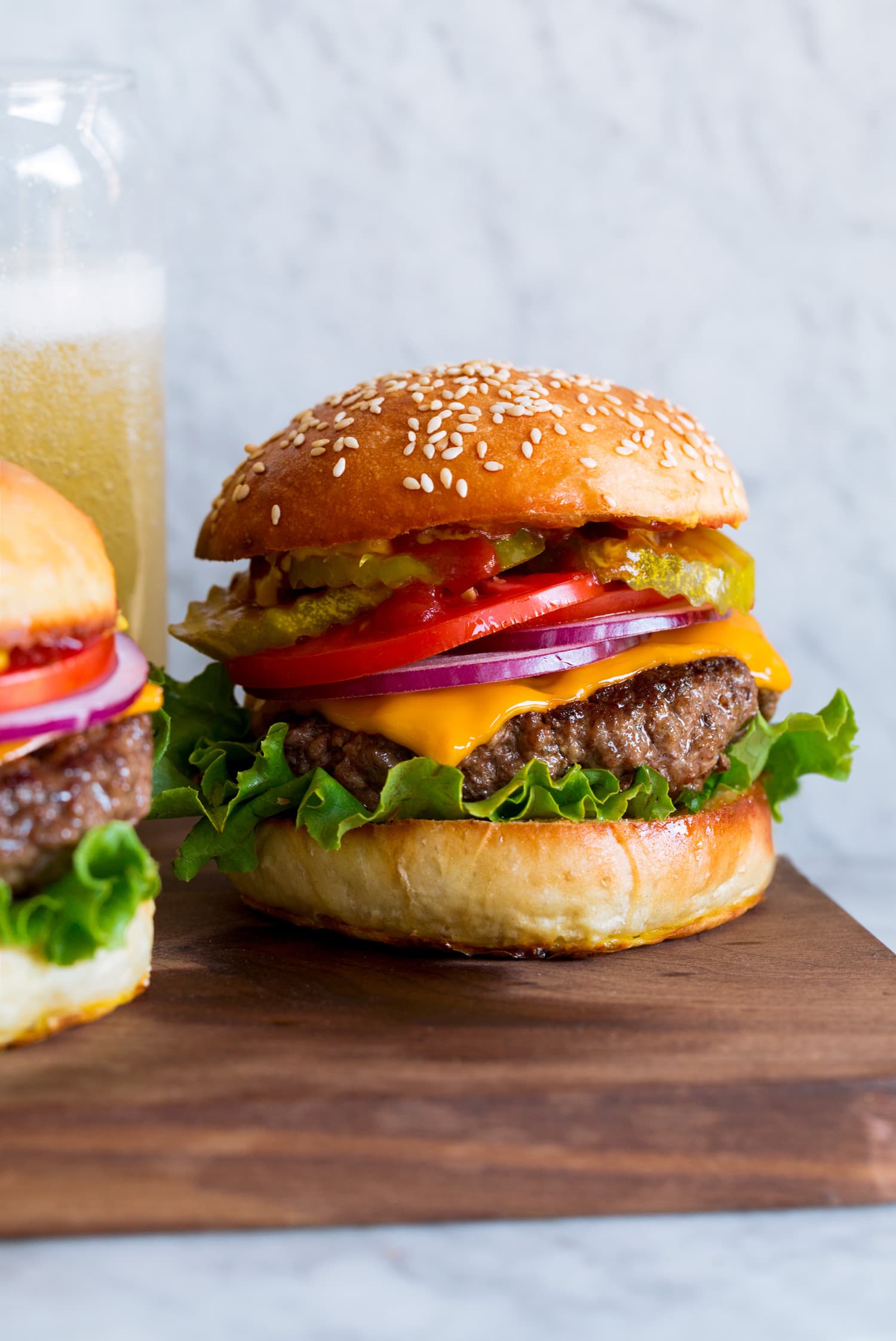 Homemade Hamburgers Hamburger shown on homemade bun with lettuce, cheddar, tomatoes and pickles.