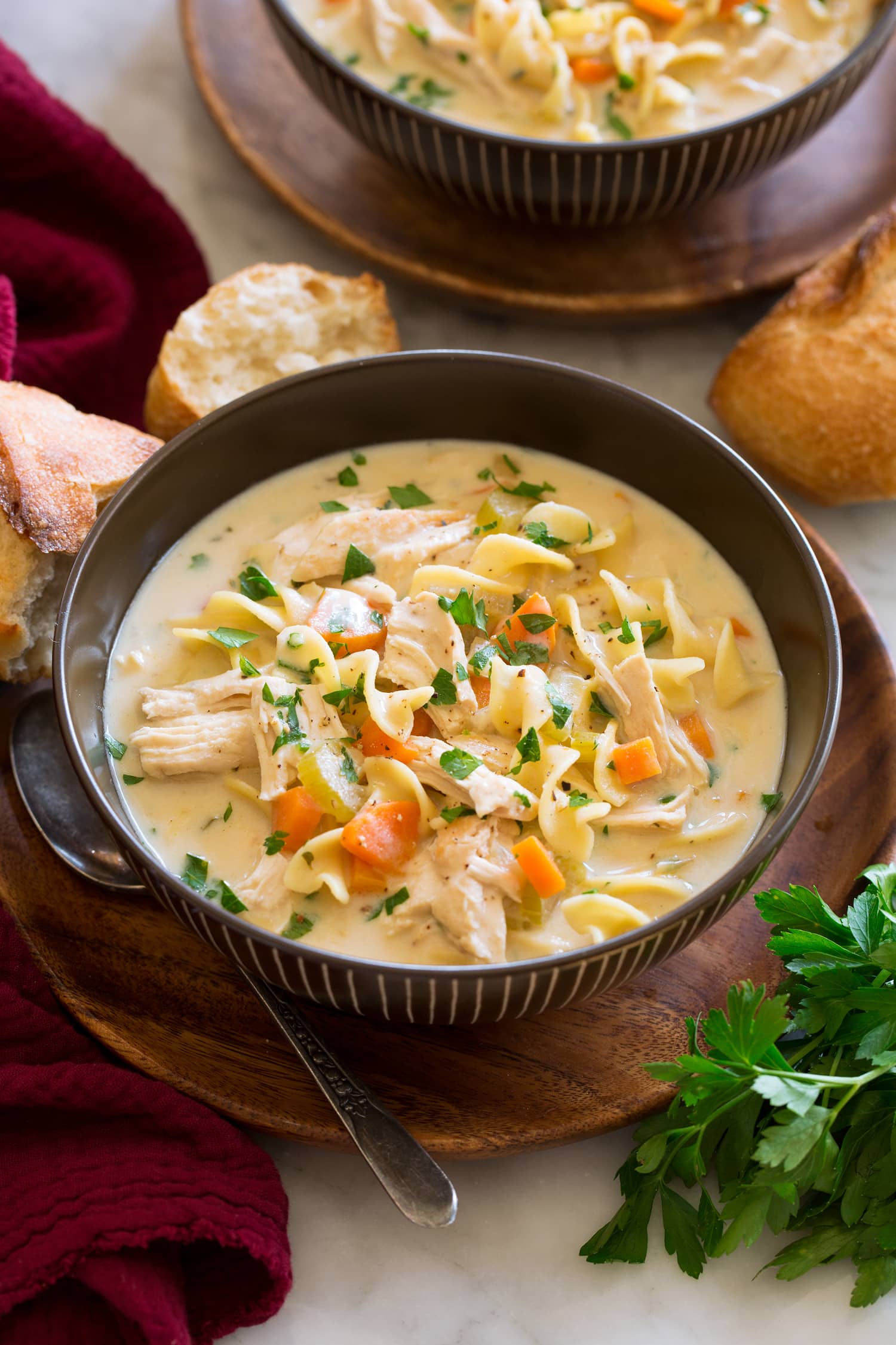 Creamy Chicken Noodle Soup Serving of creamy chicken noodle soup shown in a brown bowl over a wooden plate.