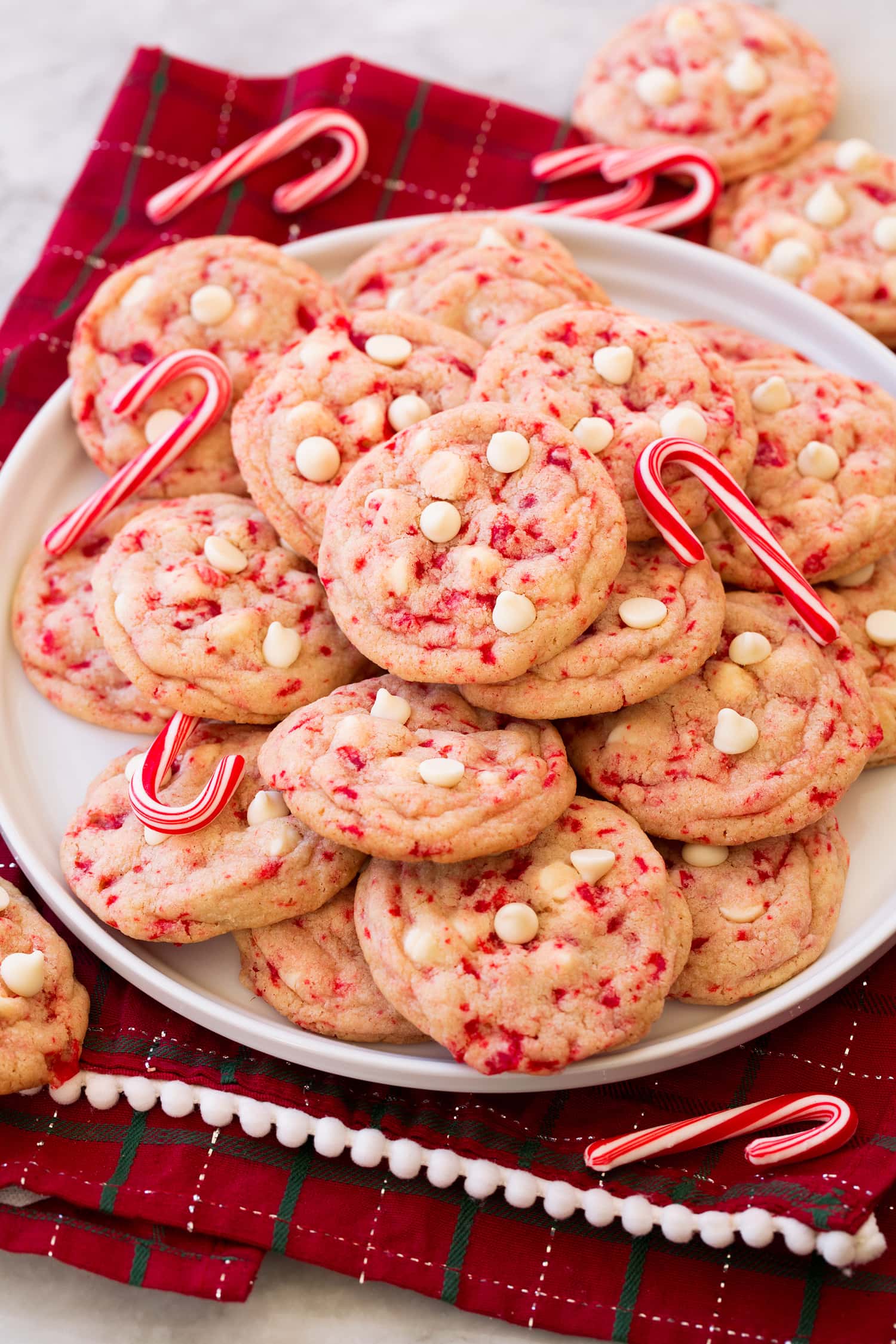 Peppermint White Chocolate Chip Cookies Peppermint white chocolate chip cookies stacked on a plate with candy canes decorating them.