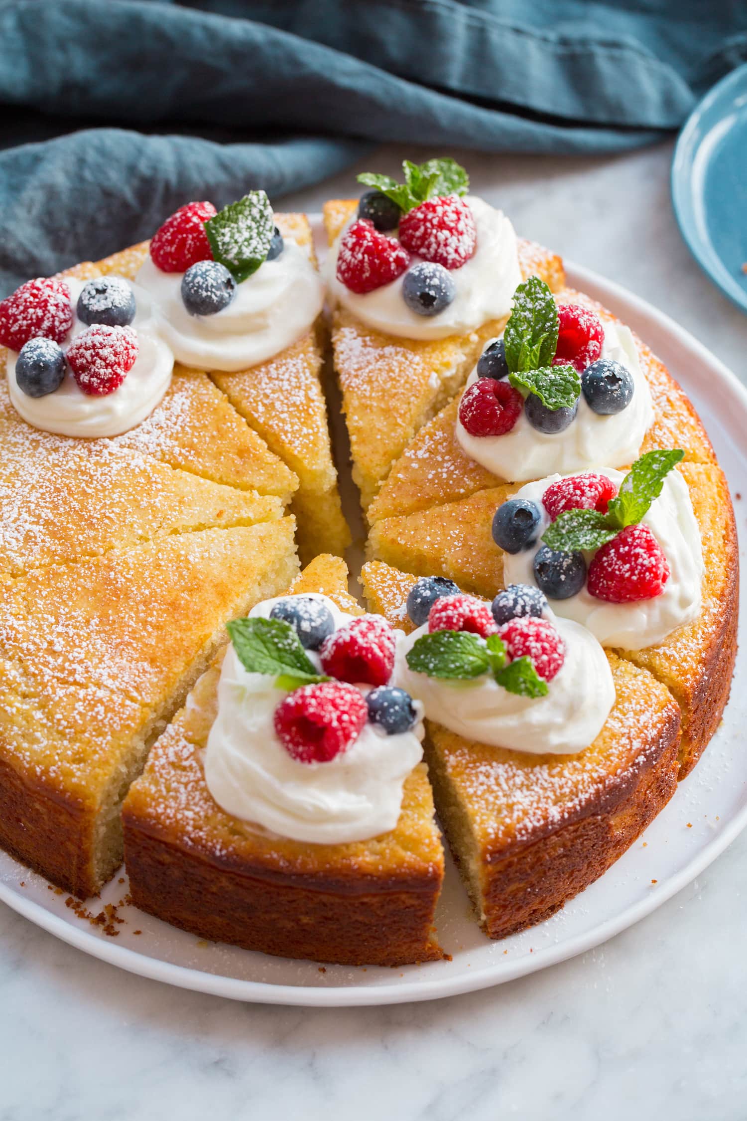 Yogurt Cake Whole yogurt cake sliced with cream and berries on top.