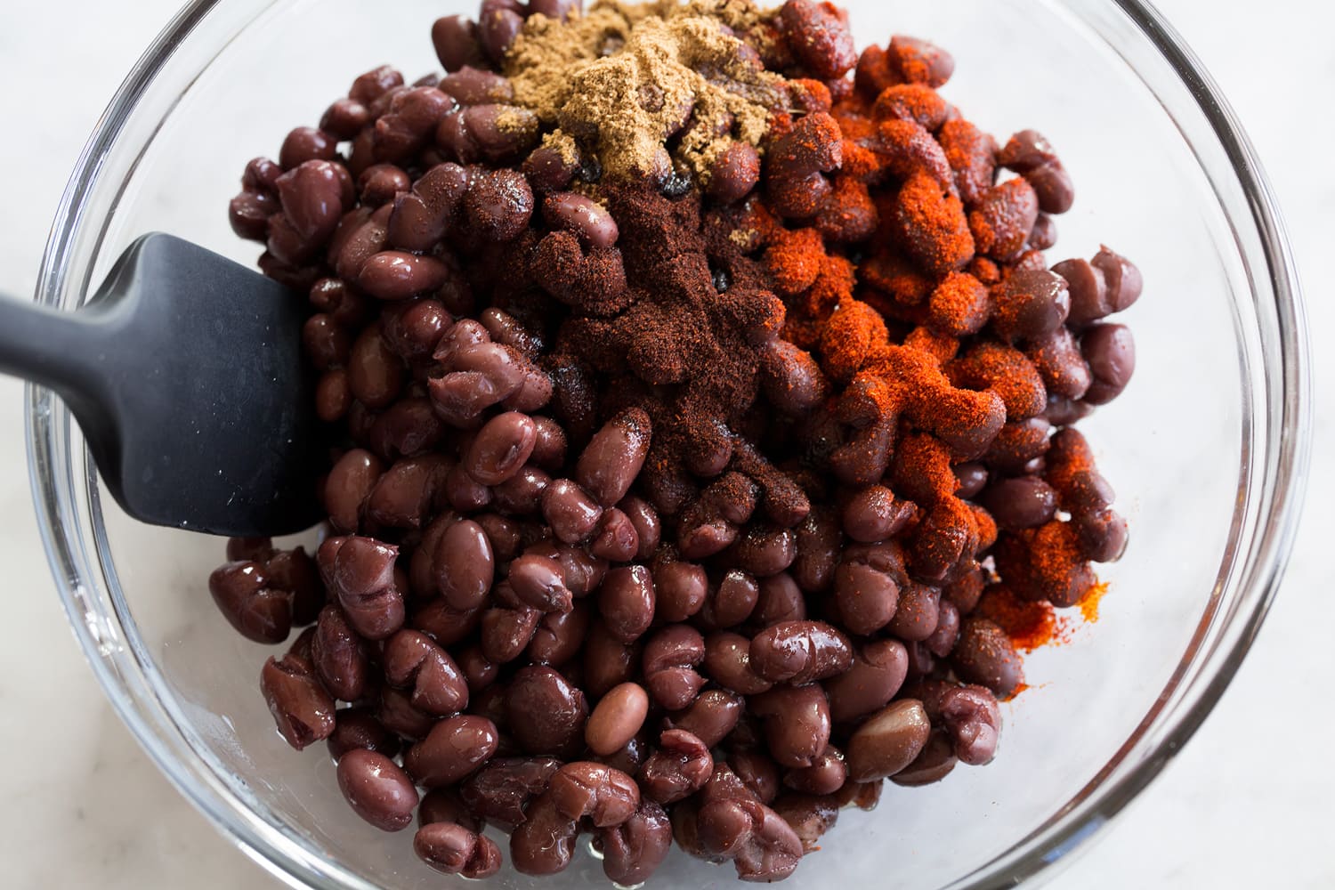 Baja Grain Bowl Black beans being tossed with spices in a mixing bowl.