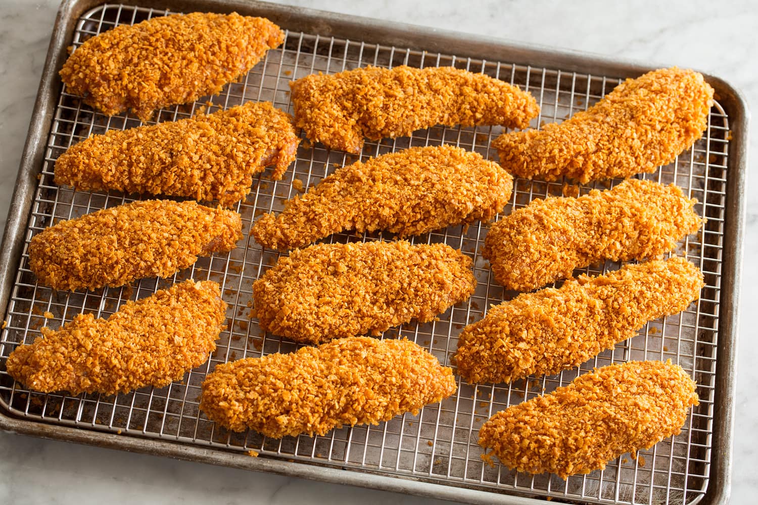 Hot Honey Chicken Chicken strips shown on a wire rack and baking sheet before baking.