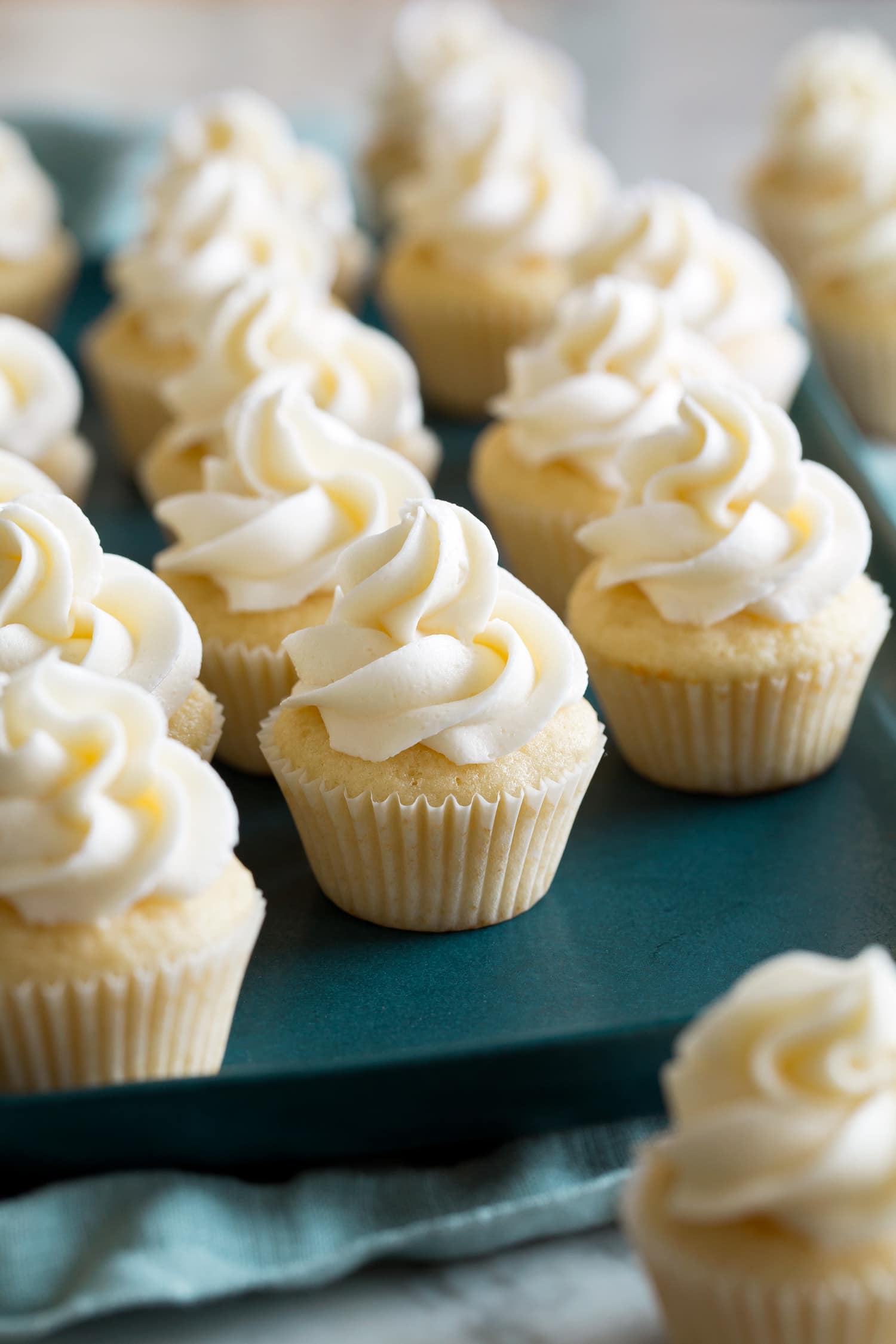Mini Cupcakes Mini vanilla cupcakes with buttercream frosting on a teal serving tray.