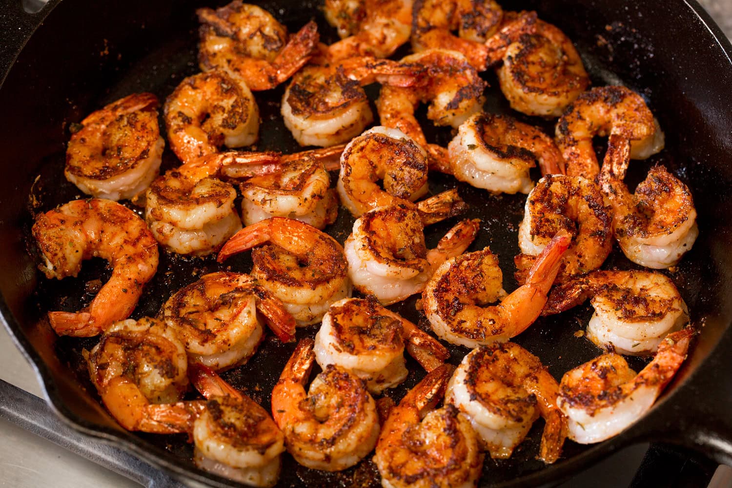 Blackened Shrimp Blackened shrimp shown cooked through in a cast iron skillet on second side.