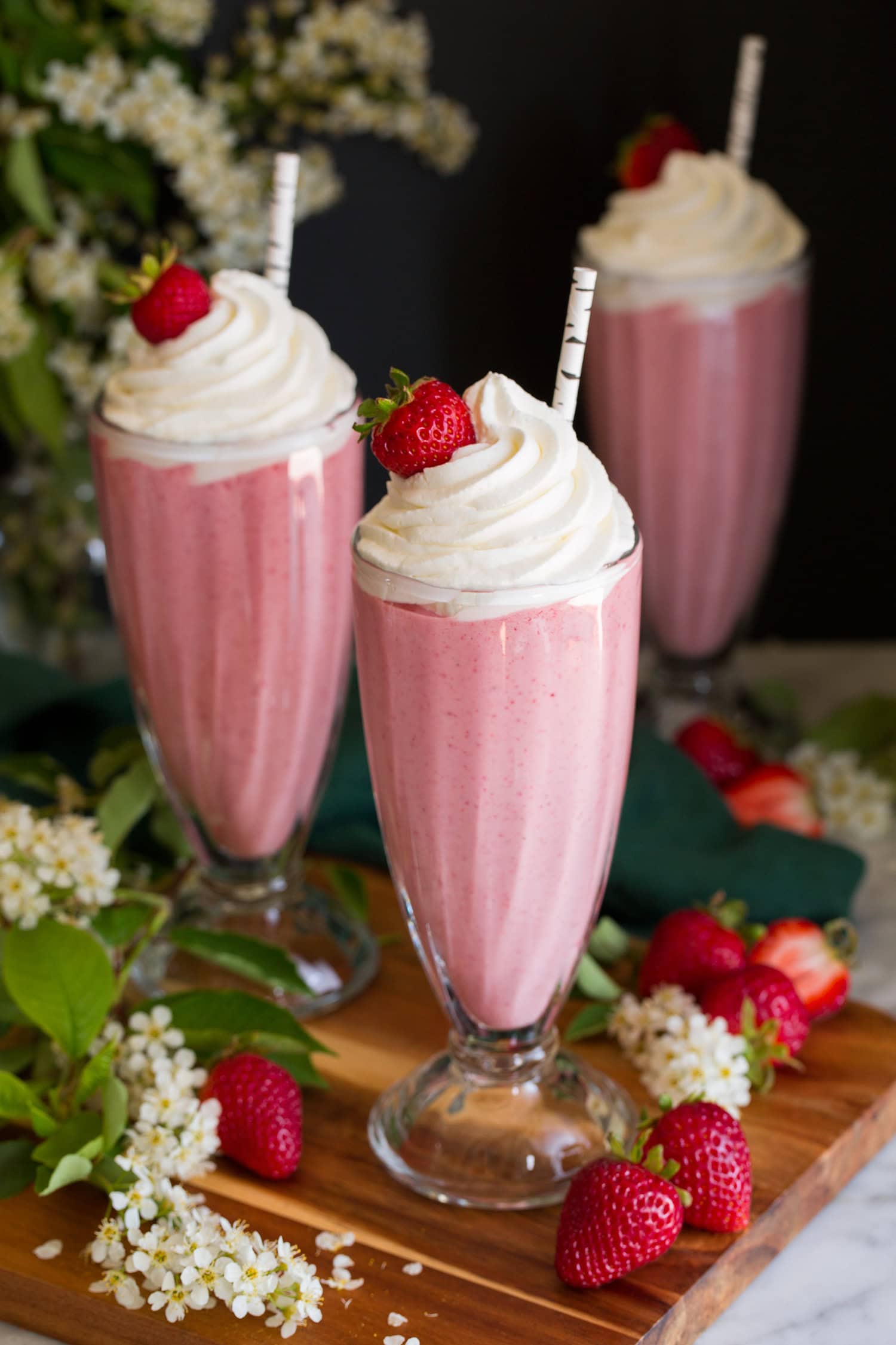 Strawberry Milkshakes Three homemade strawberry milkshakes in tall glasses topped with whipped cream and strawberries.