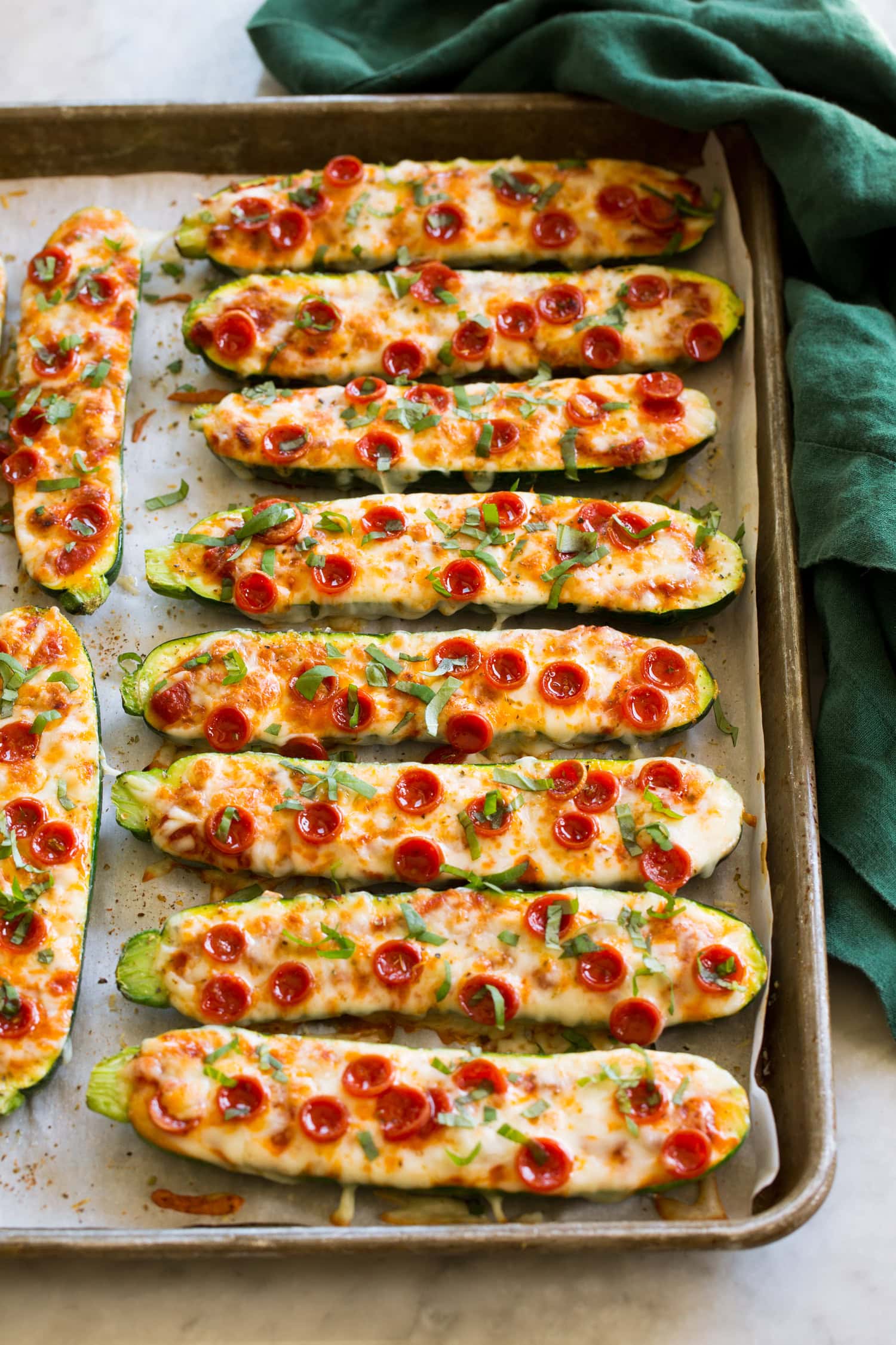 Zucchini Pizza Boats Zucchini Pizza Boats on a large baking sheet with a green cloth to the side.