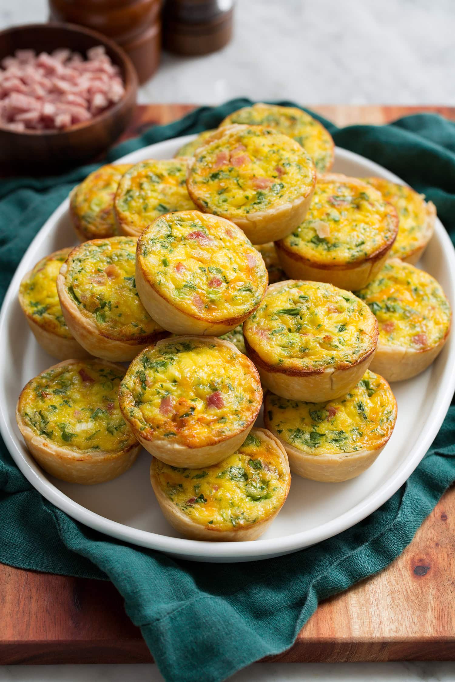 Mini Quiche Mini quiche stacked on a white oval platter over a teal cloth.