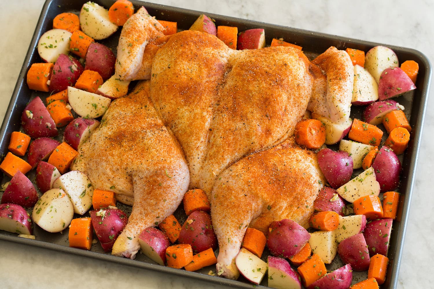 Spatchcock Chicken Spatchcock chicken and vegetables on a baking sheet shown before roasting.