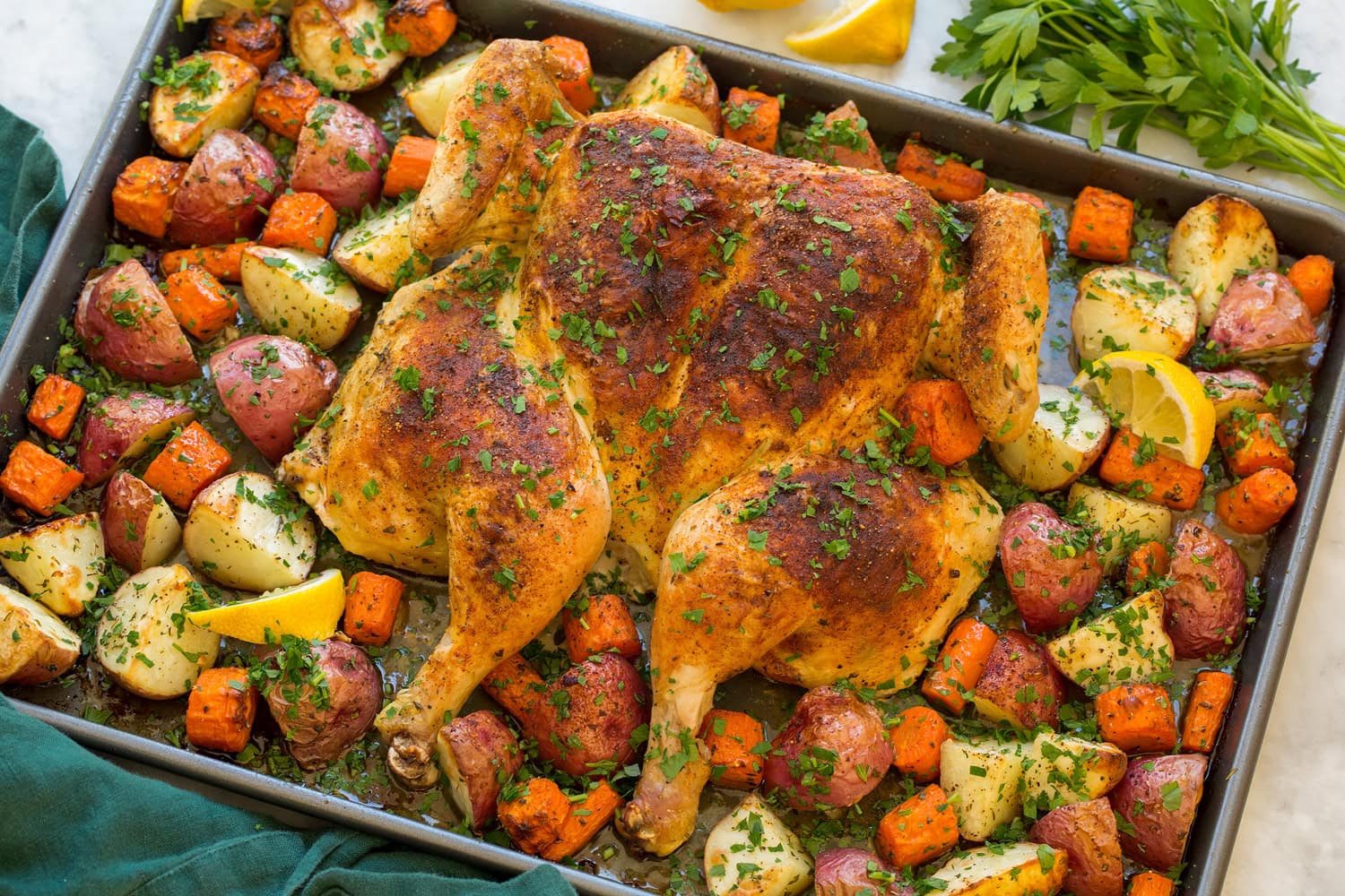 Spatchcock Chicken Spatchcock chicken and veggies on baking sheet shown after roasting.