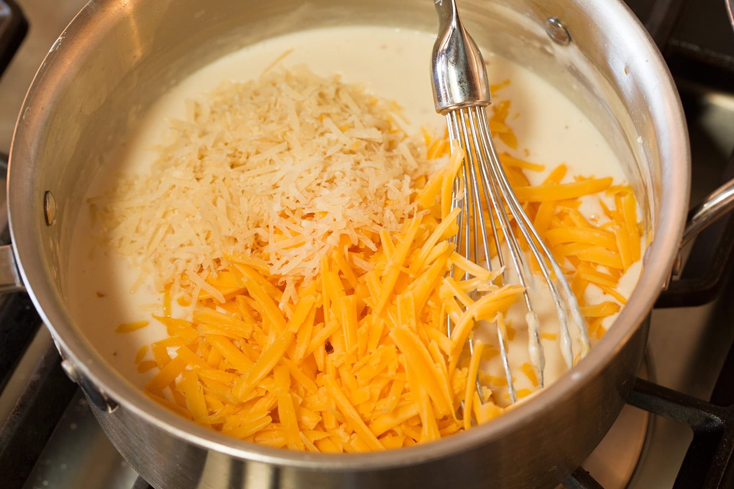 Funeral Potatoes Cheddar and parmesan added to white sauce in saucepan.